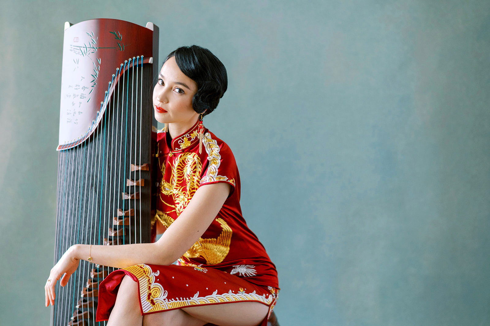 Model wearing a traditional blue silk Qipao sitting on a chair, vintage Shanghai style