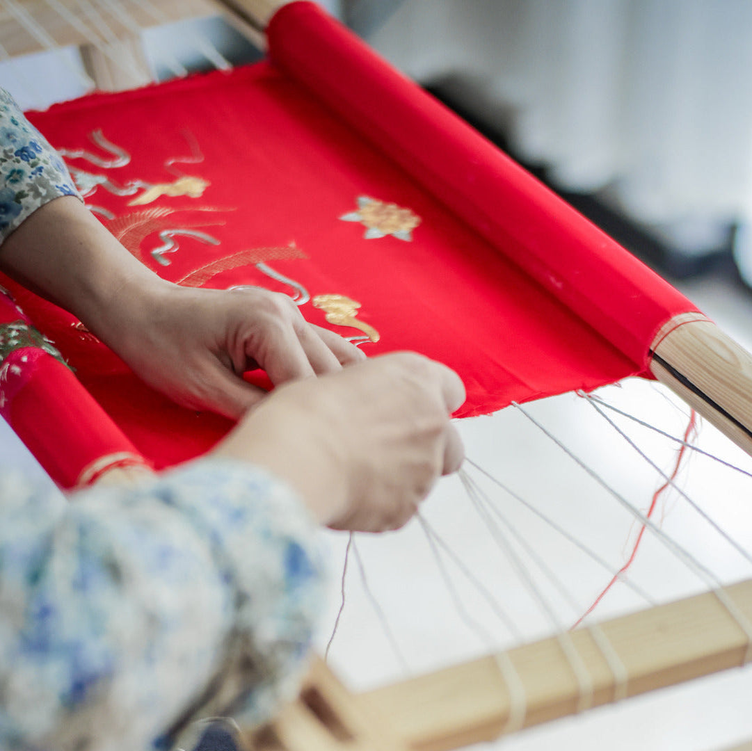 Close-up of one artisan perform finishing checks on hand embroidery before another artisan start sewing.