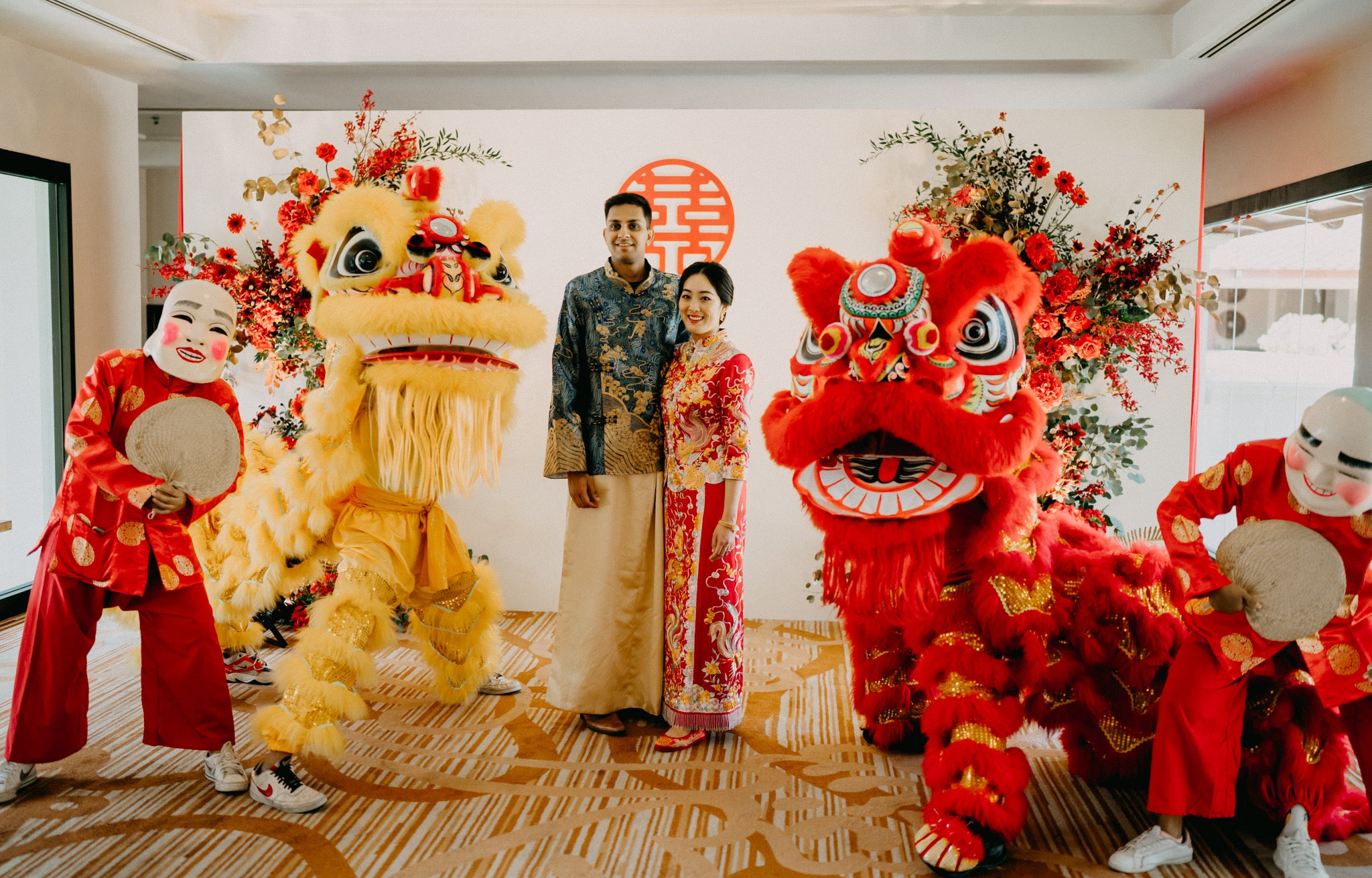 Bride Cara wearing a custom red Chinese wedding dress Qun Kwa with dragon and phoenix embroidery beside her groom in a matching teal green Tang suit, both designed by JINZA Oriental Couture.