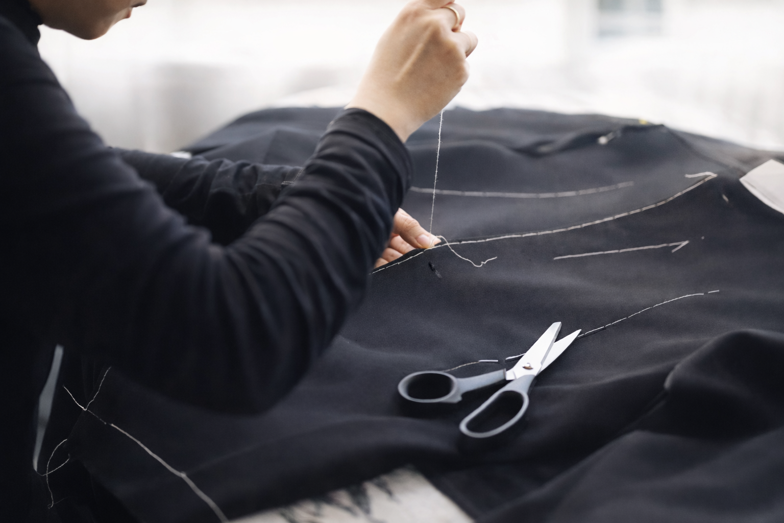 Designer adjusting muslin fitting for a custom Tang suit using hand stitching in Los Angeles studio.
