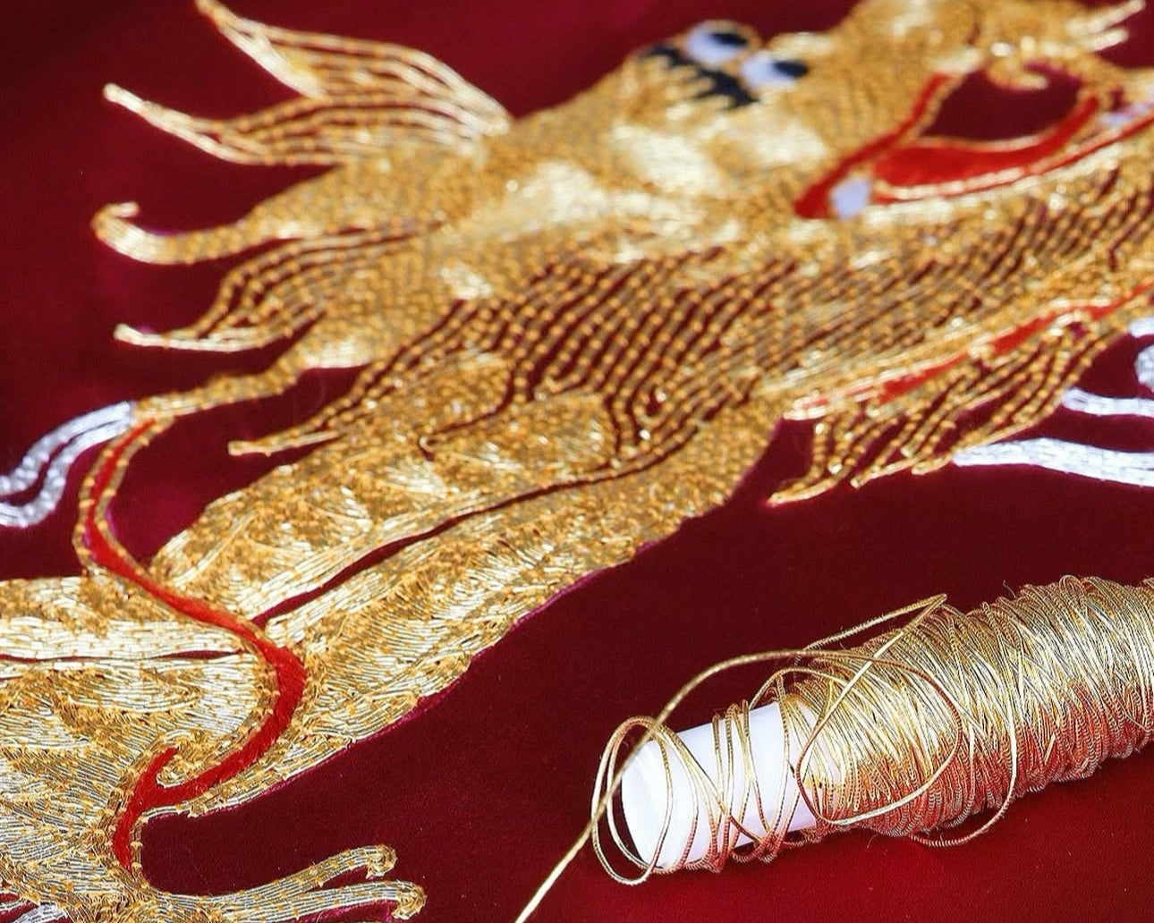 Close-up of a gold hand-embroidered dragon with a spool of thread imported from Japan.