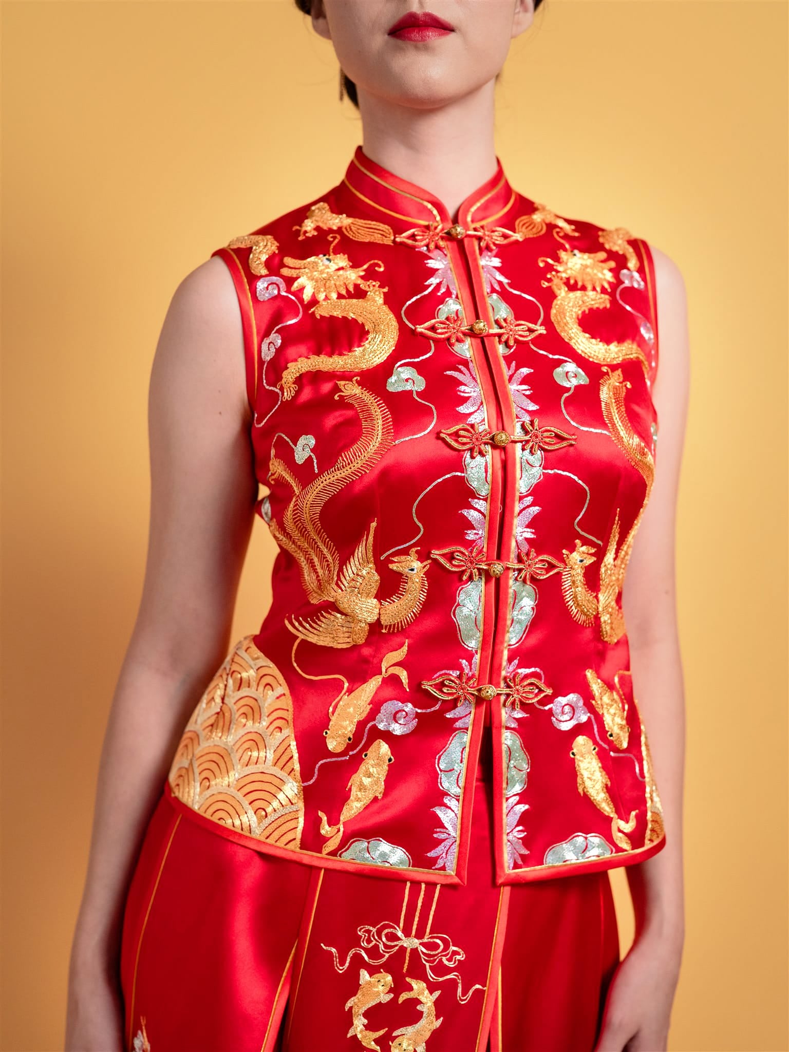 Close-up of gold hand embroidery featuring phoenix, dragon, lotus, and peonies on red silk Chinese wedding dress skirt