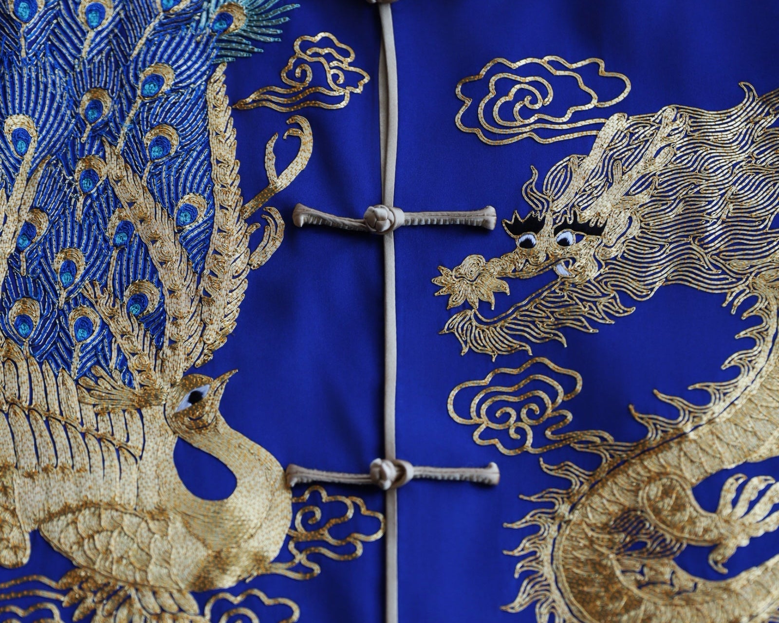 Navy blue Tang suit for groom with gold dragon and peacock embroidery, symbolizing strength, harmony, and cultural unity.