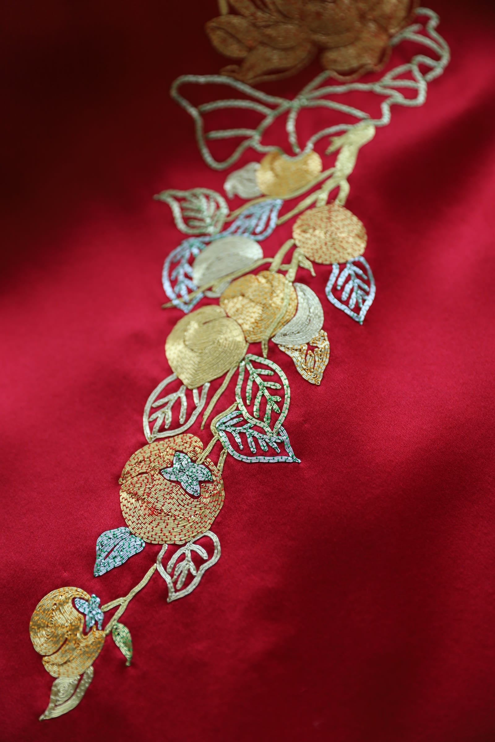Close up of gold pomegranate and butterfly hand embroidery on red silk Qipao, symbol of fertility and joy, available at JINZA Los Angeles