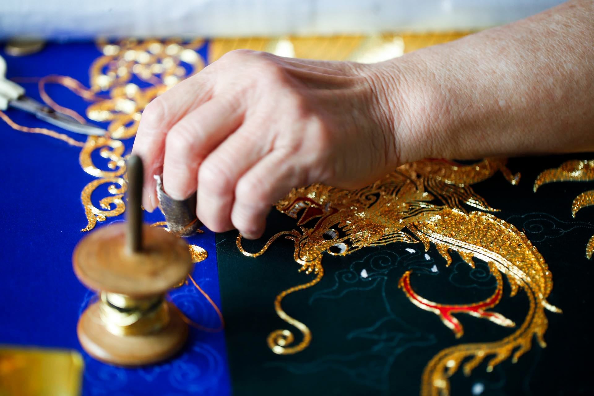 Chinese artisan hand-embroidering dragon motif on wedding Qipao using gold threads