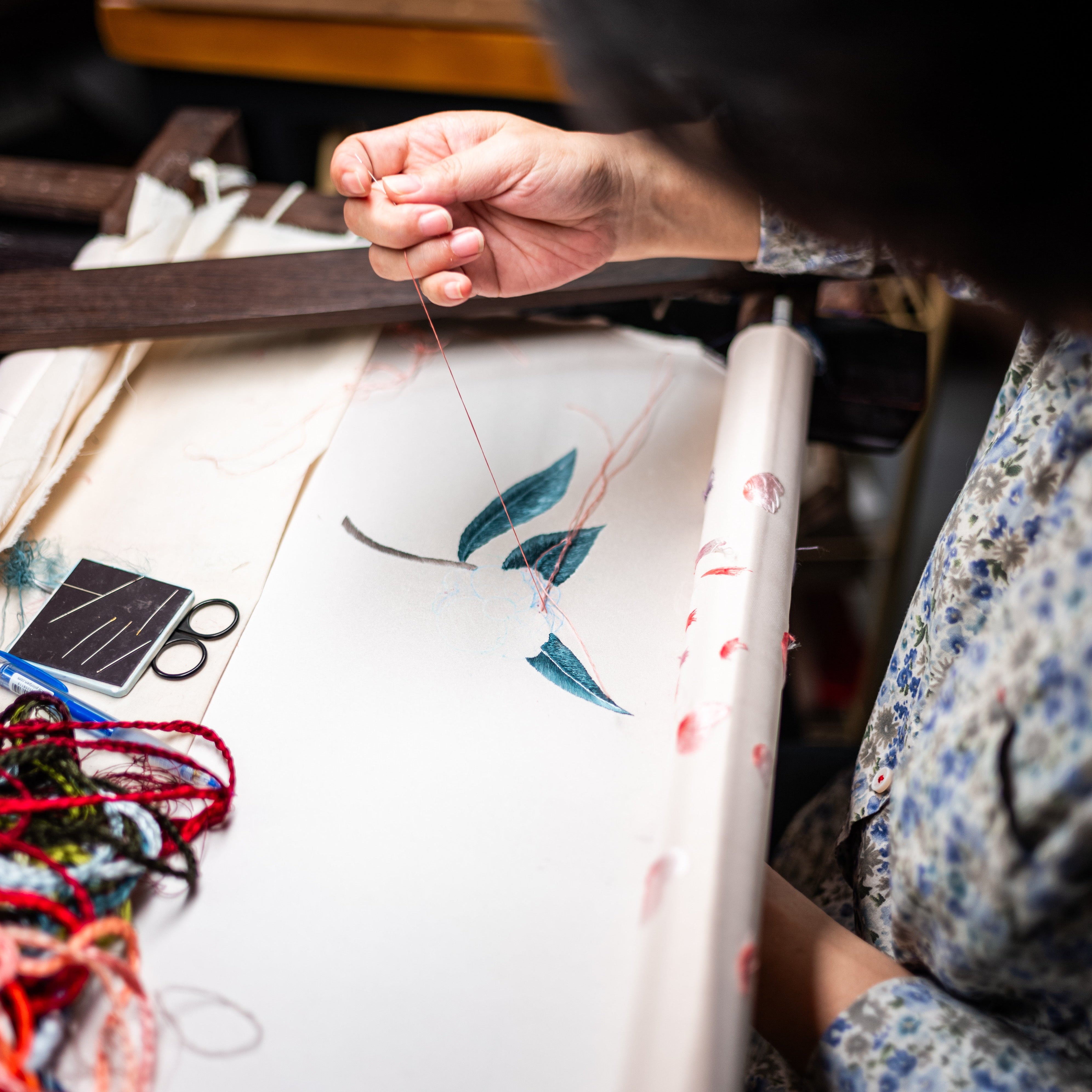 A woman is doing hand embroidery for a custom-made wedding Qipao