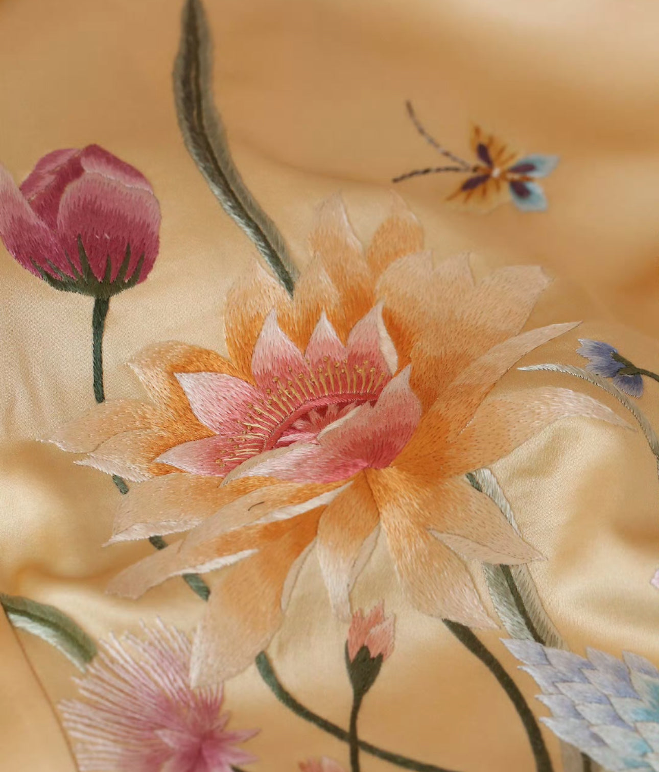 A close-up of a hand-embroidered peony flower in gold and pink threads on a soft gold silk Qipao. 