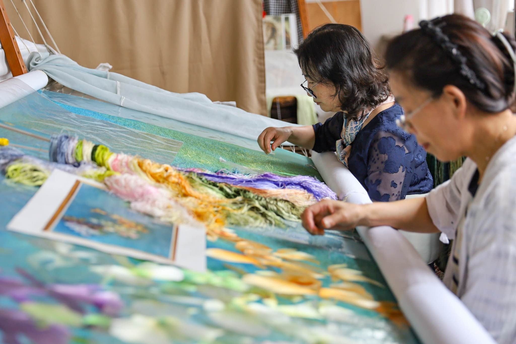 Two artisans working on a large embroidery table at JINZA atelier, handcrafting cultural symbols.