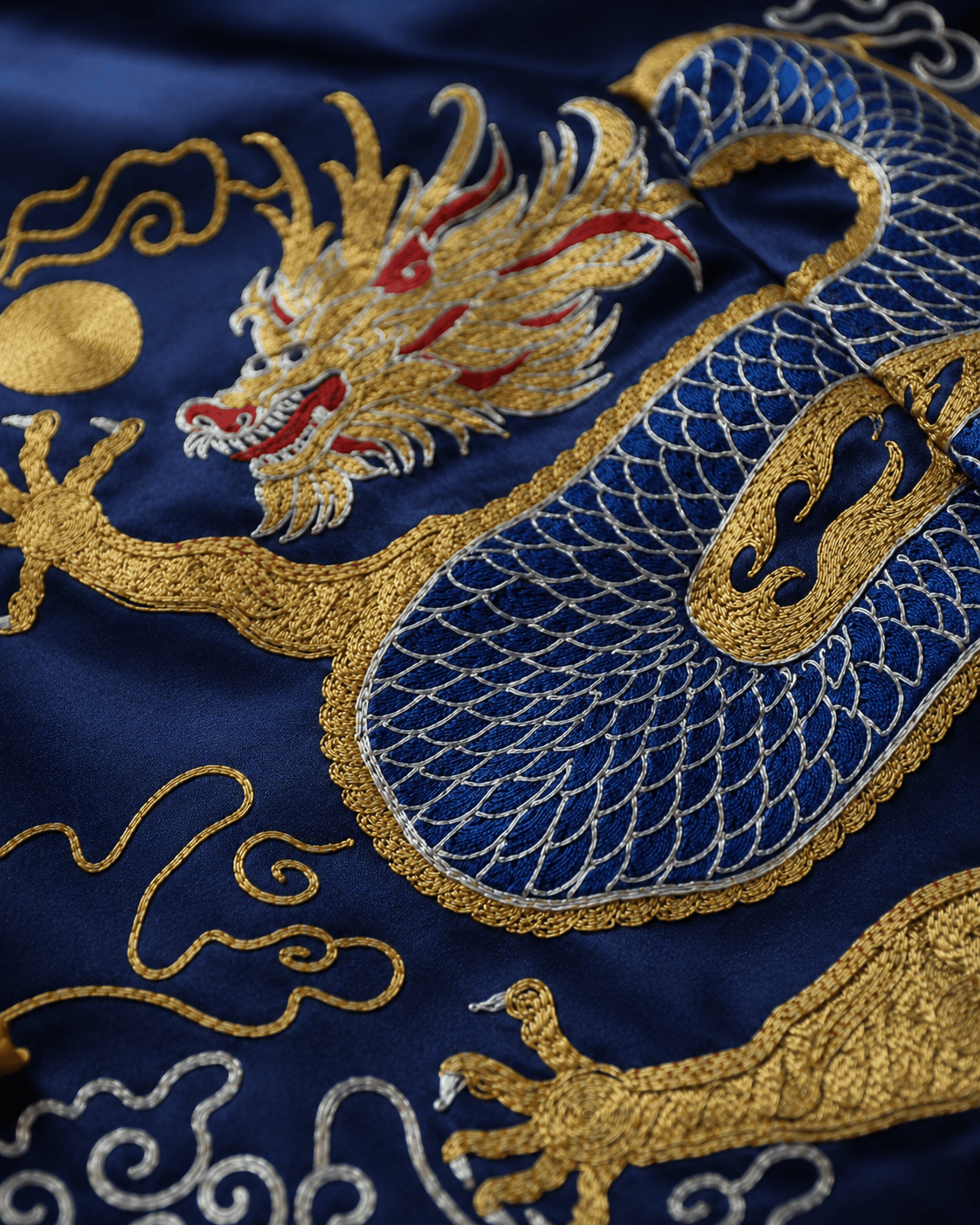 Close up of gold and blue dragon hand embroidery with red accents and gold sun on bespoke navy silk Tang suit, custom made at JINZA Los Angeles
