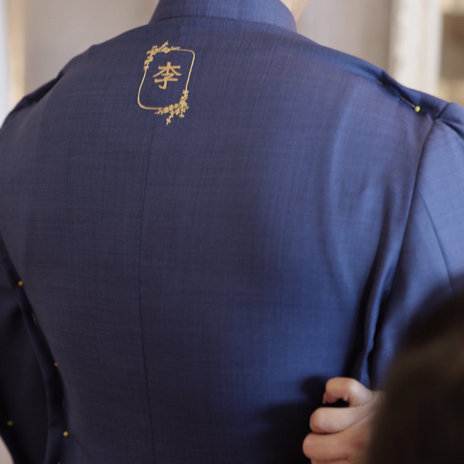 JINZA designer fitting bespoke Zhongshan suit on groom with family name embroidery on back, Los Angeles atelier