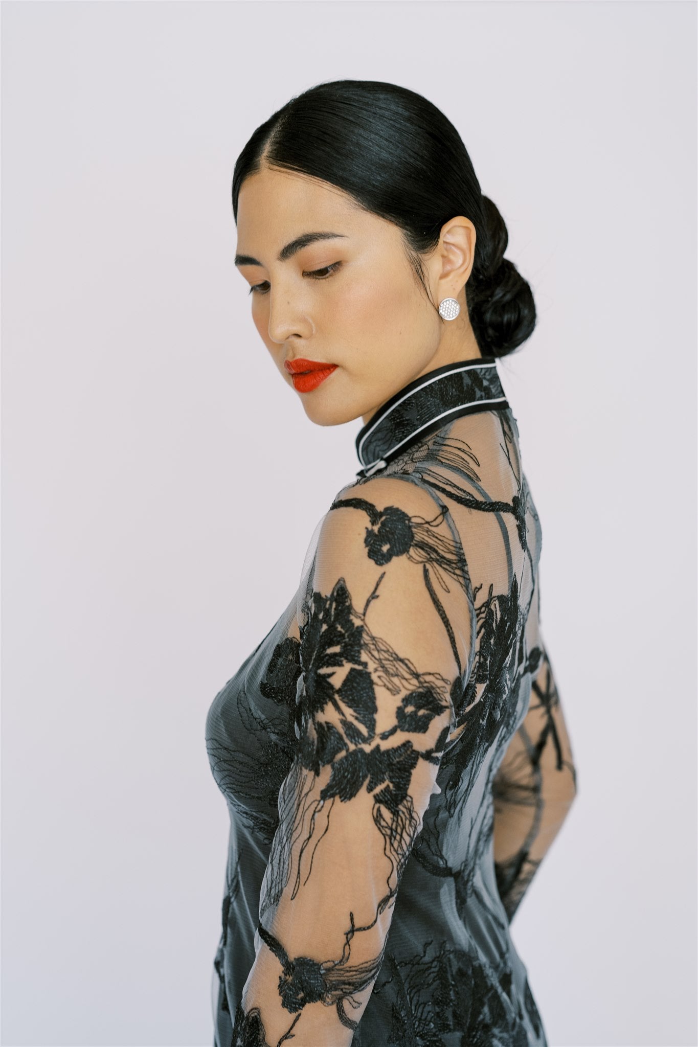 A woman is wearing pearl earrings to match black lace cheongsam