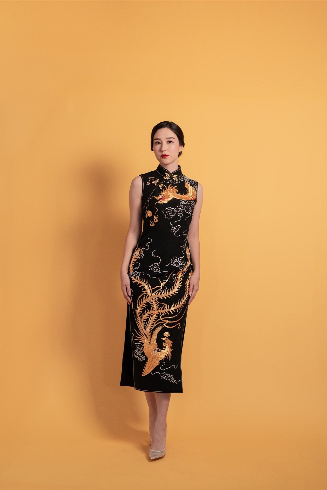 Black silk cheongsam with hand-embroidered dragon and phoenix, shown on gold background