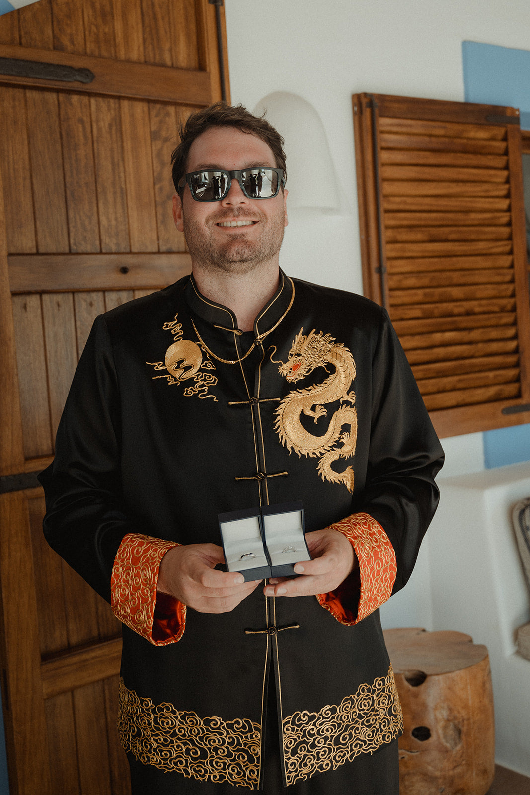 Front view of a groom wearing a custom-designed black silk tang suit for groom, featuring gold dragon, moon, lucky cloud, red calf. 