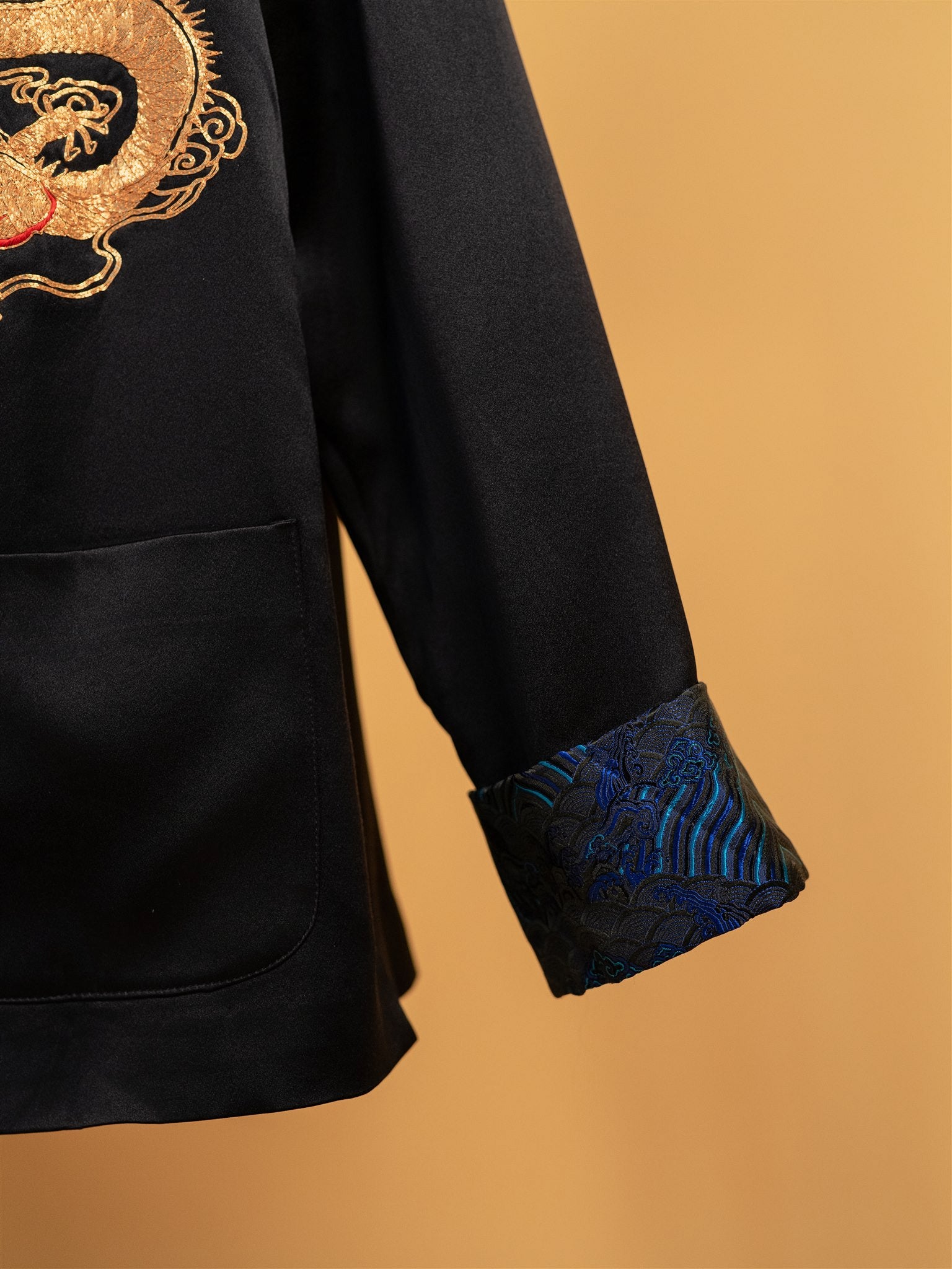 Close-up detail of the blue brocade calf on a black silk Tang suit jacket designed for special occasions.