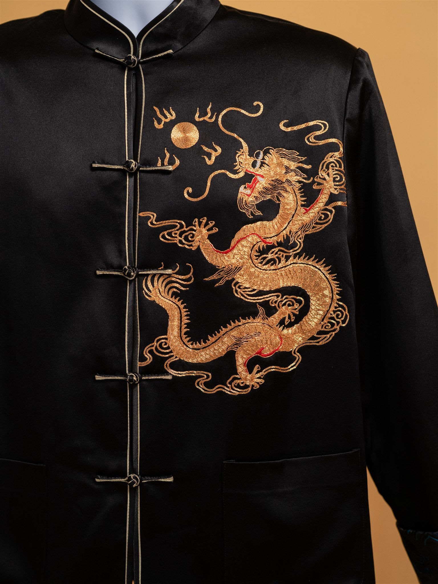 Close-up detail of the gold dragon hand embroidery on a black silk Tang suit jacket designed for special occasions.