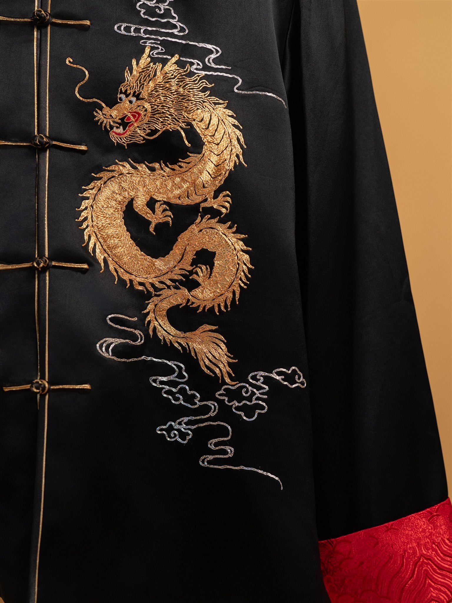 Front view of a black silk Tang suit with red brocade cuffs, gold dragon embroidery, and gold Pankou knots, designed for a groom.