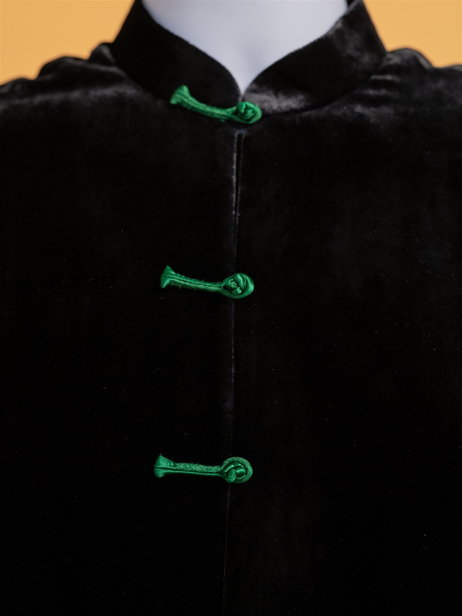 A detailed view of the green frot knot buttons on a black silk velvet tang suit. 