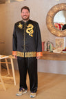 A groom is wearing a black tang suit jacket with gold dragon and cloud embroidery with matching silk pants