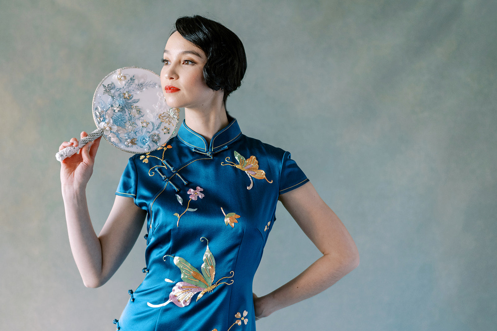 Close-up of butterfly and peony hand embroidery on teal blue silk Qipao