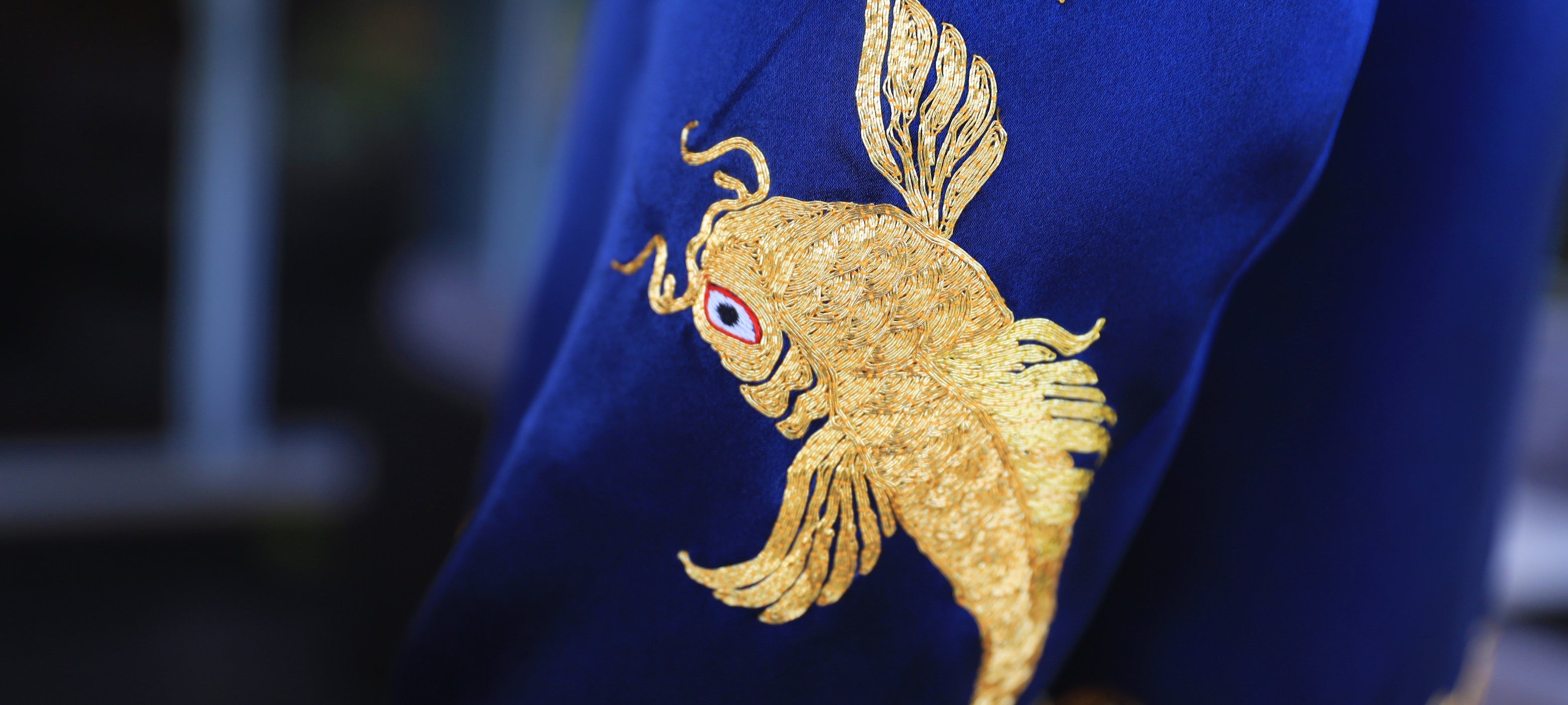 Detailed image of a hand-embroidered koi fish in gold thread on a blue Chinese Mandarin jacket's sleeve.