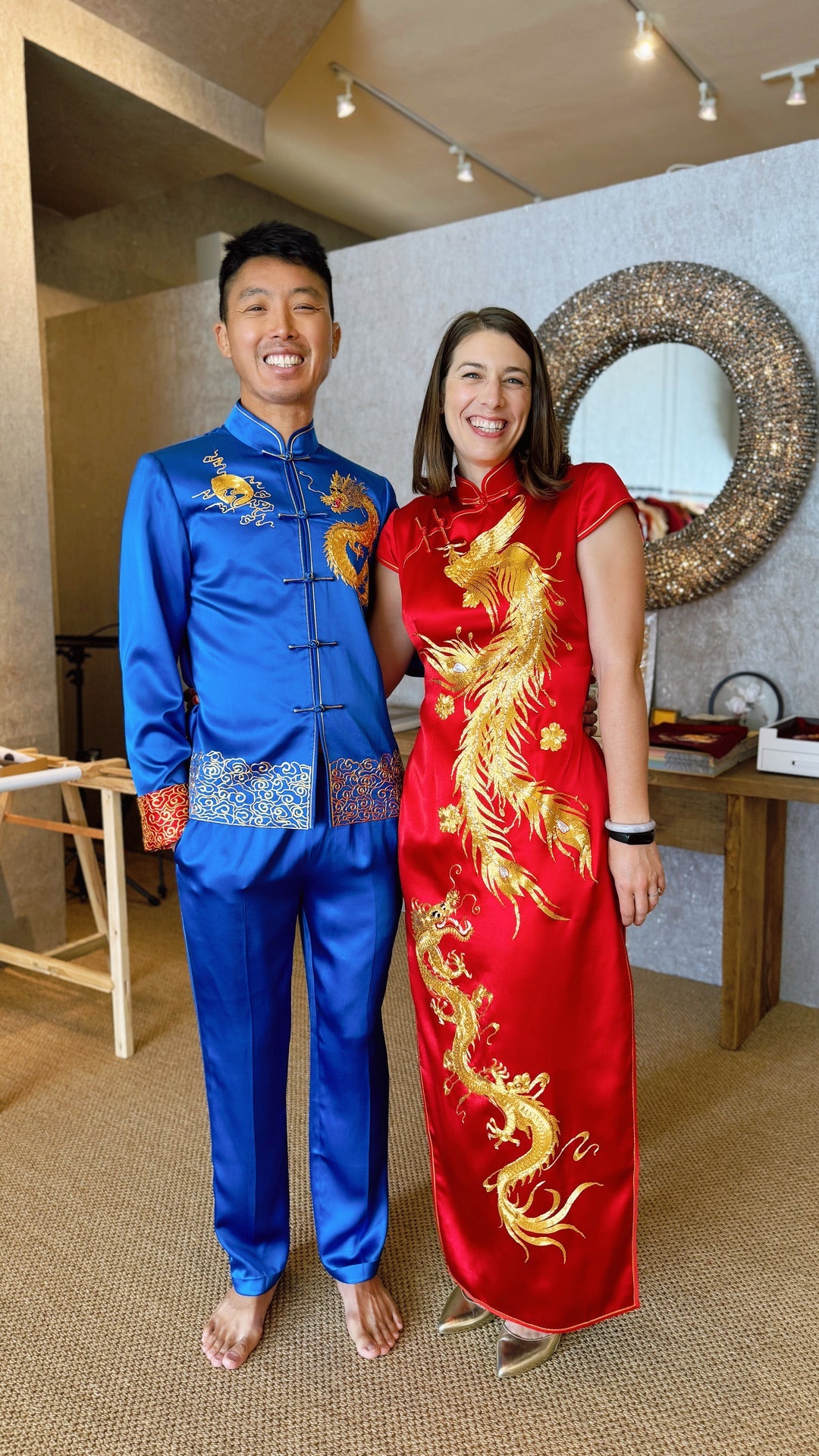 A groom wearing royal blue Tang Suit and a bride wearing a red Wedding Qipao with gold phoenix and dragon embroidery