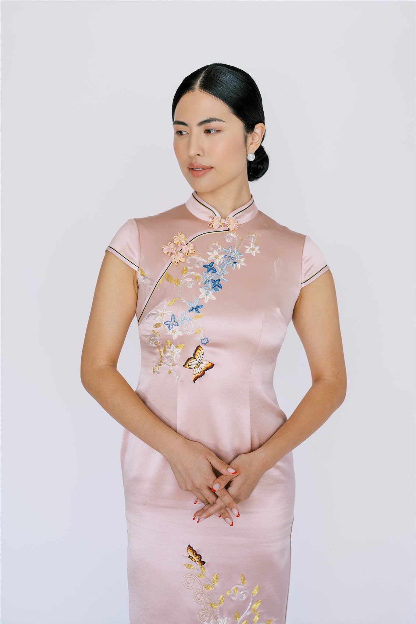 A woman wearing a pink cheongsam with blue, silver, yellow flowers embroidery