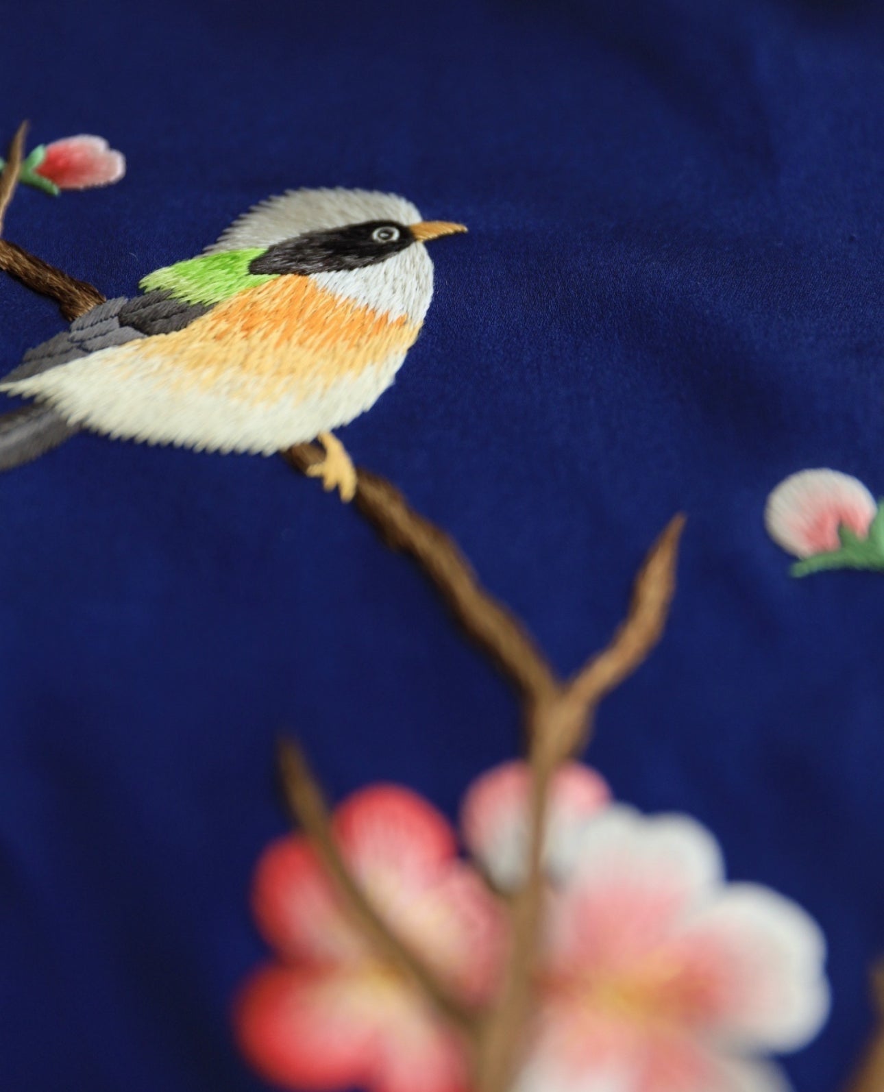 Close-up details of a bird standing on a branch of cherry blossom details on silk Qipao.