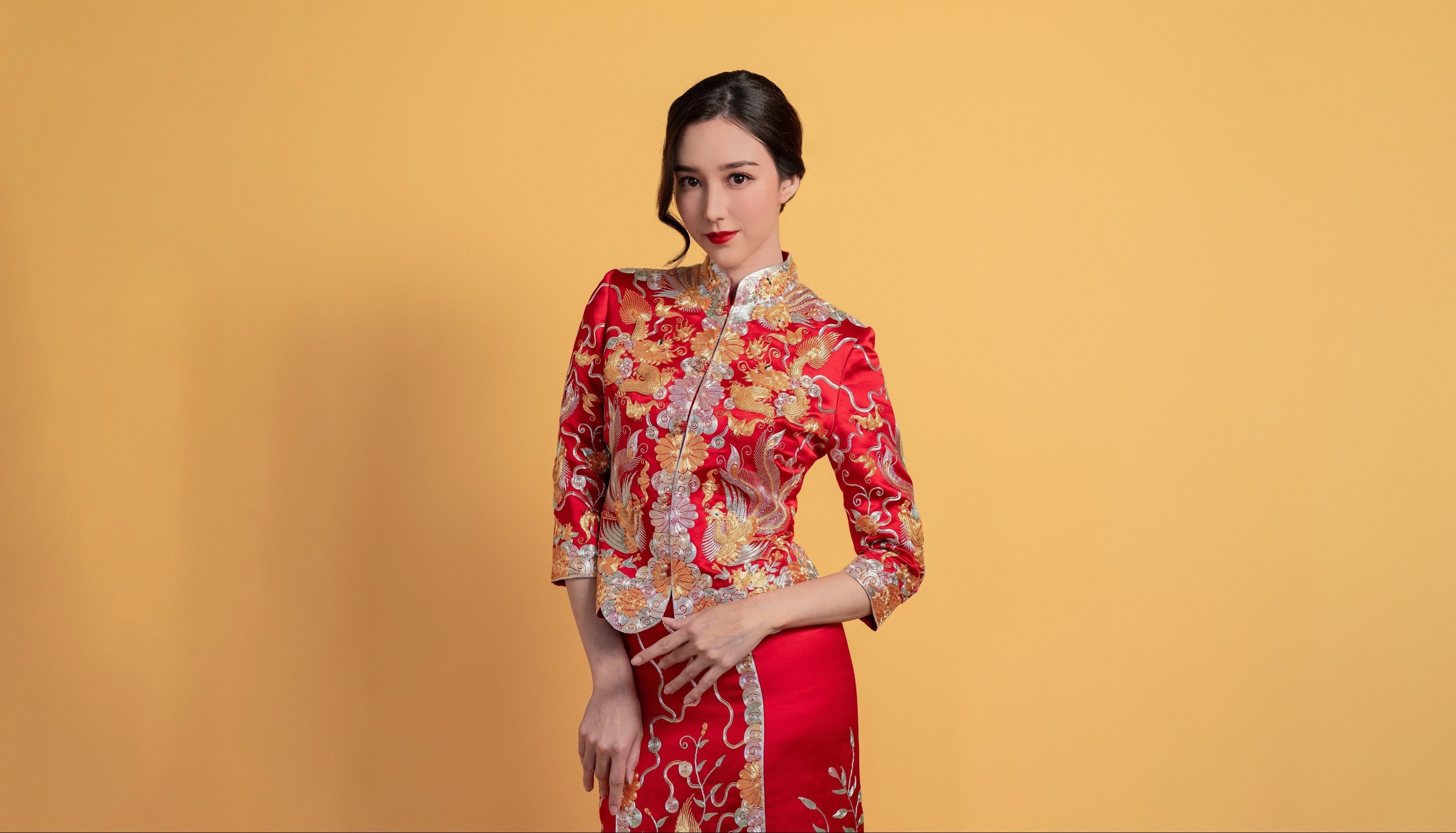 Front view of a woman wearing Chinese Wedding Dress red Qun Kwa, featuring gold and silver dragon and phoenix 3-d embroidery, for her Chinese Tea Ceremony. 