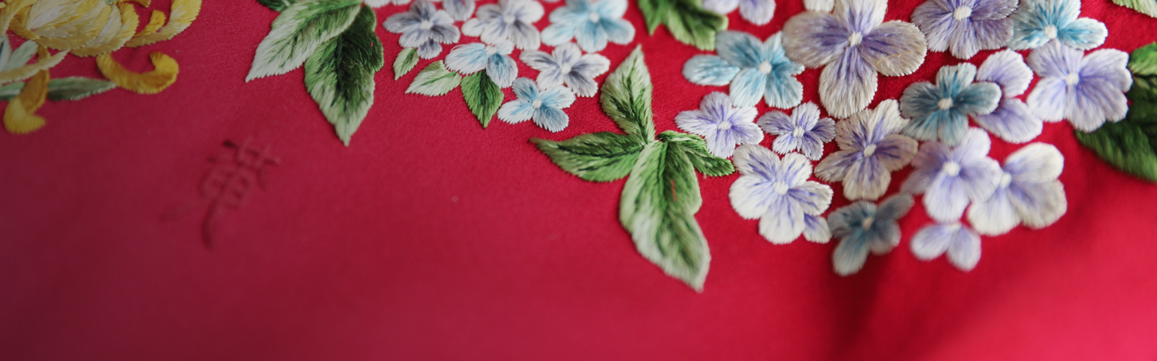 Close-up of hand-embroidered flowers and family name on a red wedding Qipao