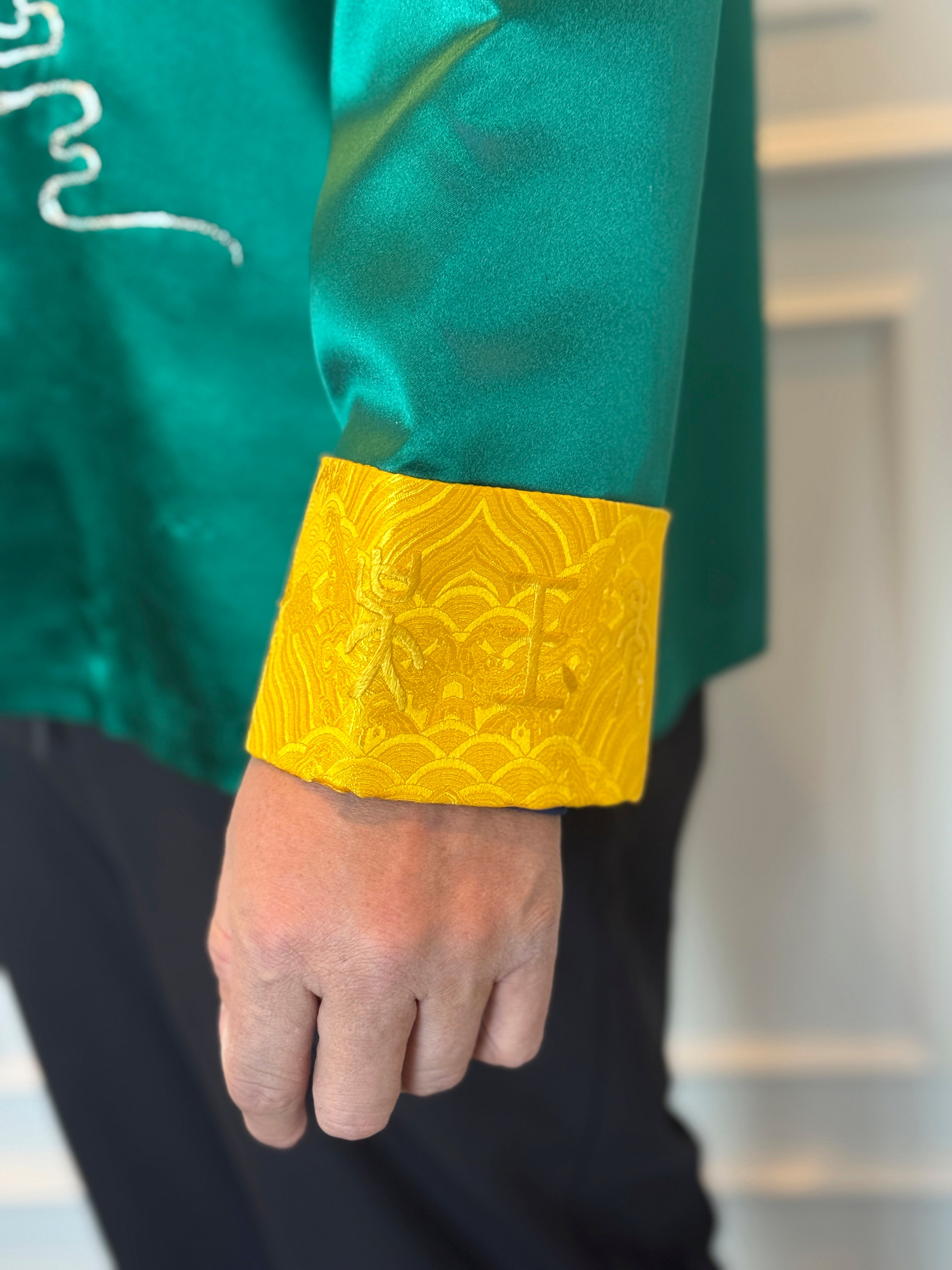 A details image of a family name hand embroidery on the left calf of a green silk tang suit. 