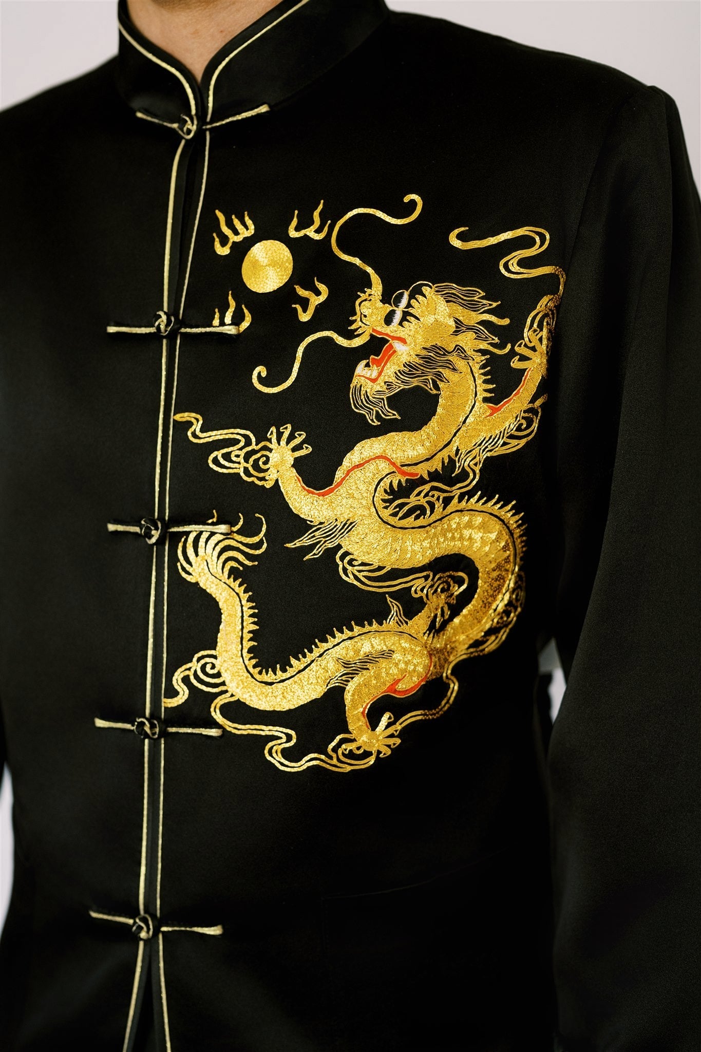 A man wearing a black silk Chinese suit with gold dragon embroidered on the chest