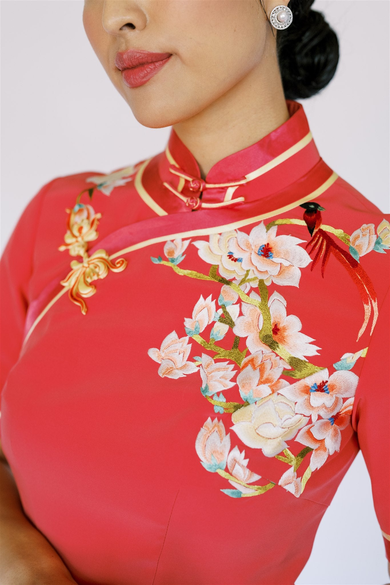 A woman wearing orange silk Qipao with hand-weaven floral pankou knot and magnolia flower