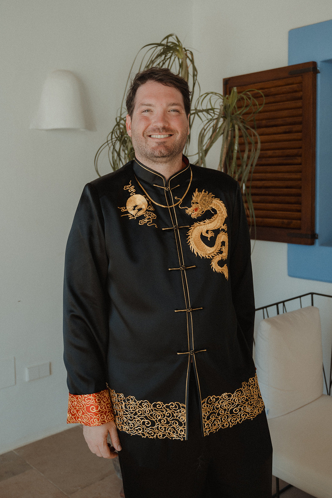 A groom is smiling in his black silk tang suit at his wedding in Spain. 