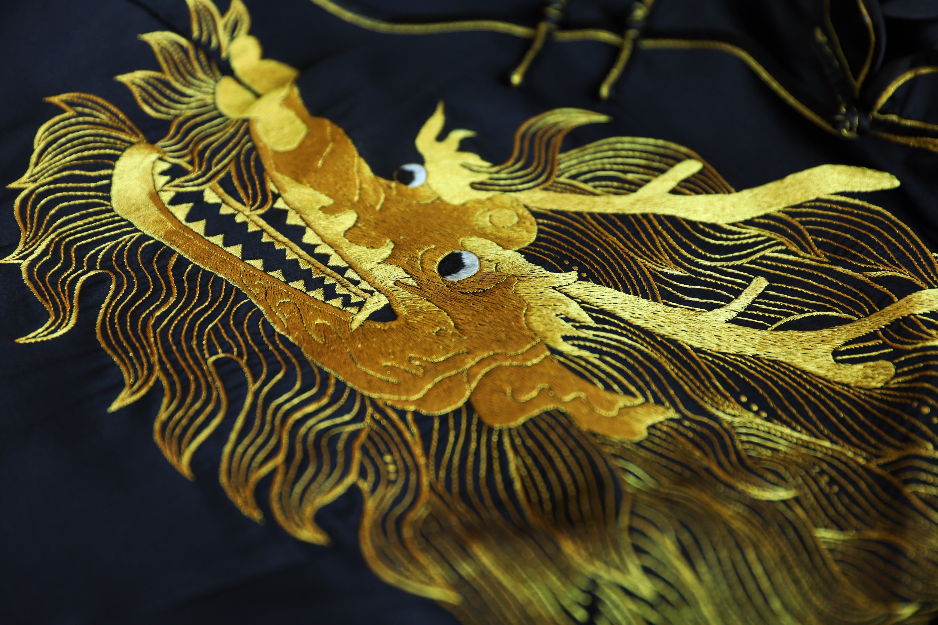 Close-up detail of gold hand embroidered dragon on a black silk Qipao.