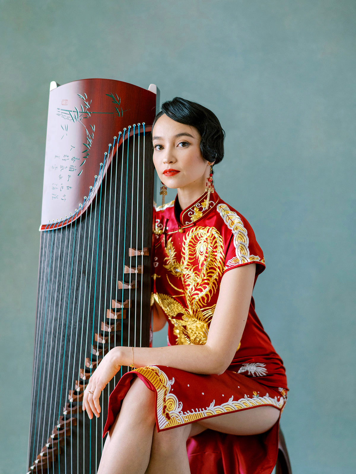 Woman in gold embroidered Chinese wedding Qipao seated with Gu Zheng, showing elegant silhouette