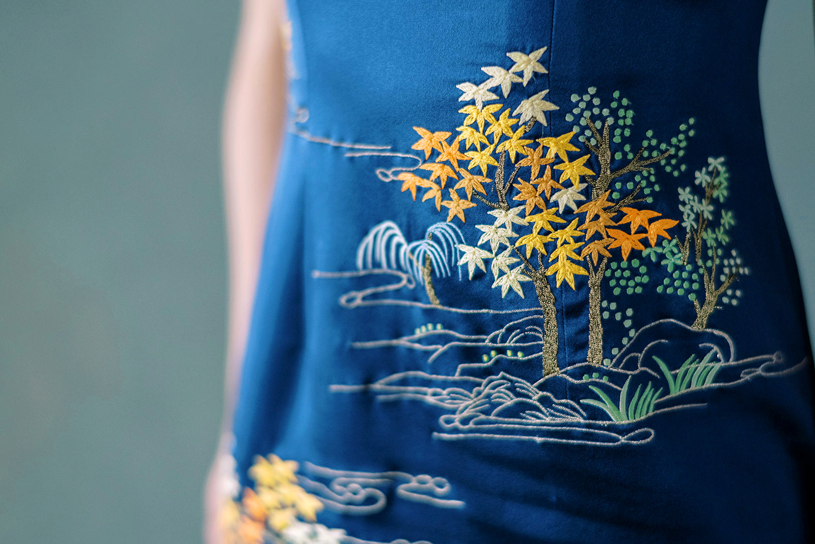 Close-up of hand embroidery on Qipao featuring trees, rocks, and mountain scene in silk thread
