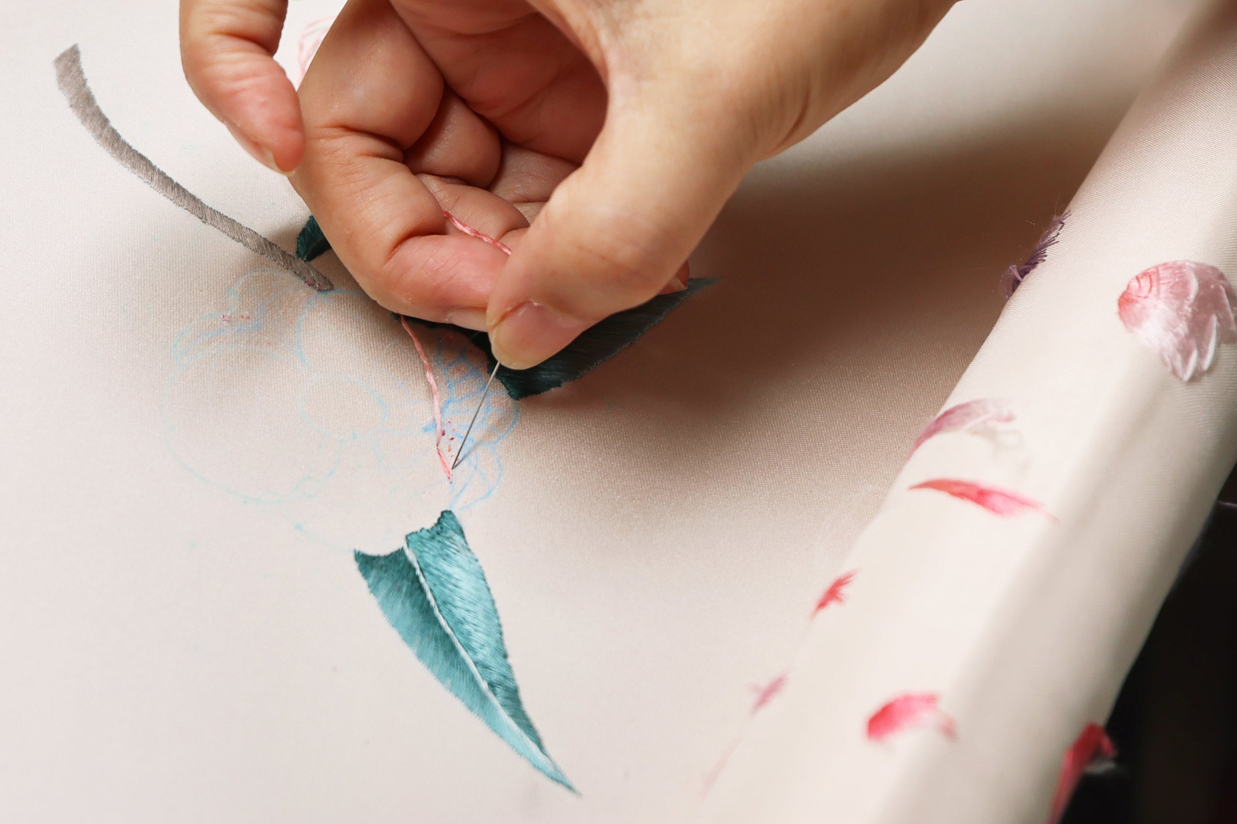 Close-up of artisan hand embroidering leaf pattern on ivory silk Qipao