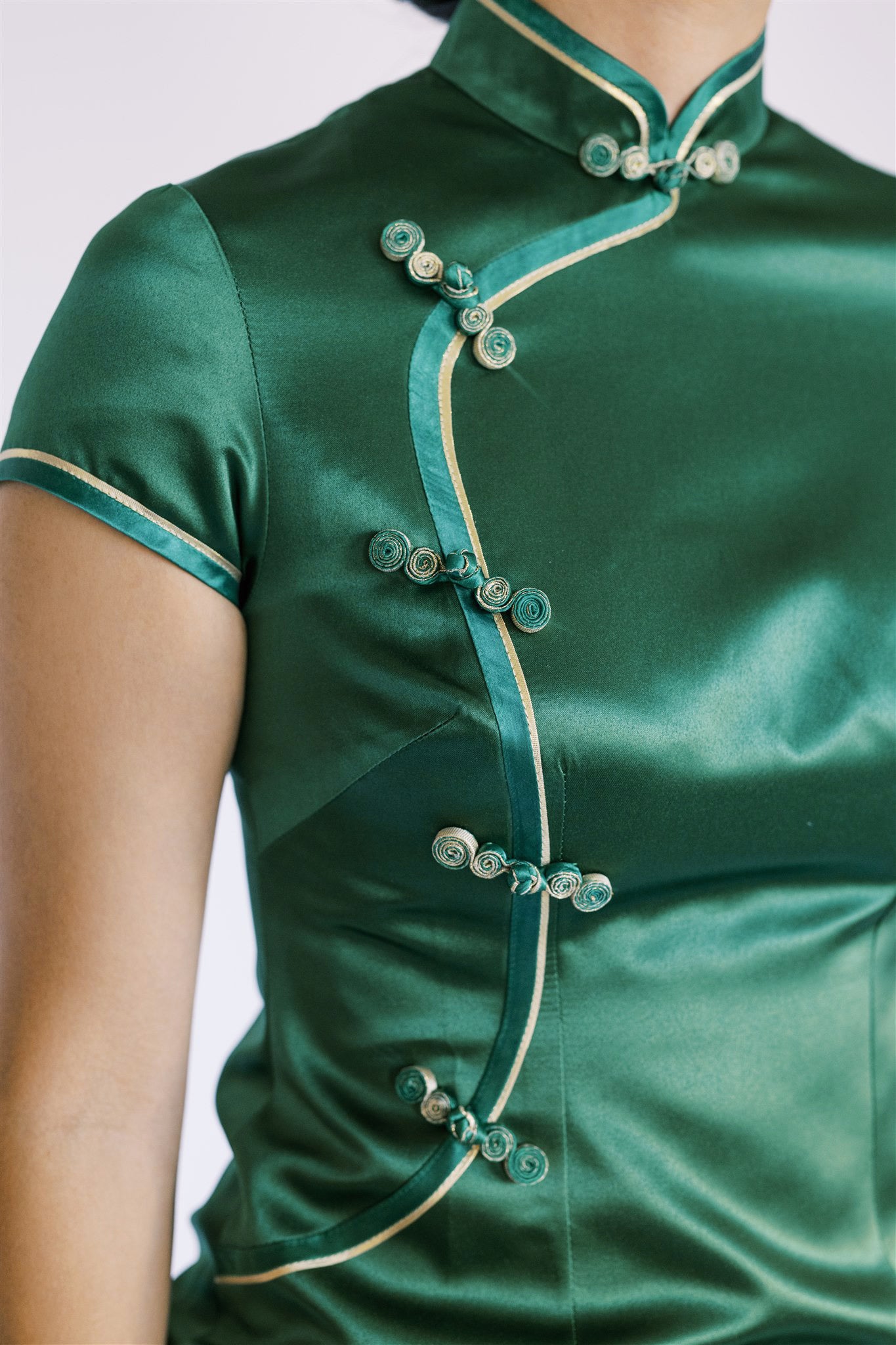 Close-up of details of traditional hand-weaven Pankou knot and gold trim on a green cheongsam.