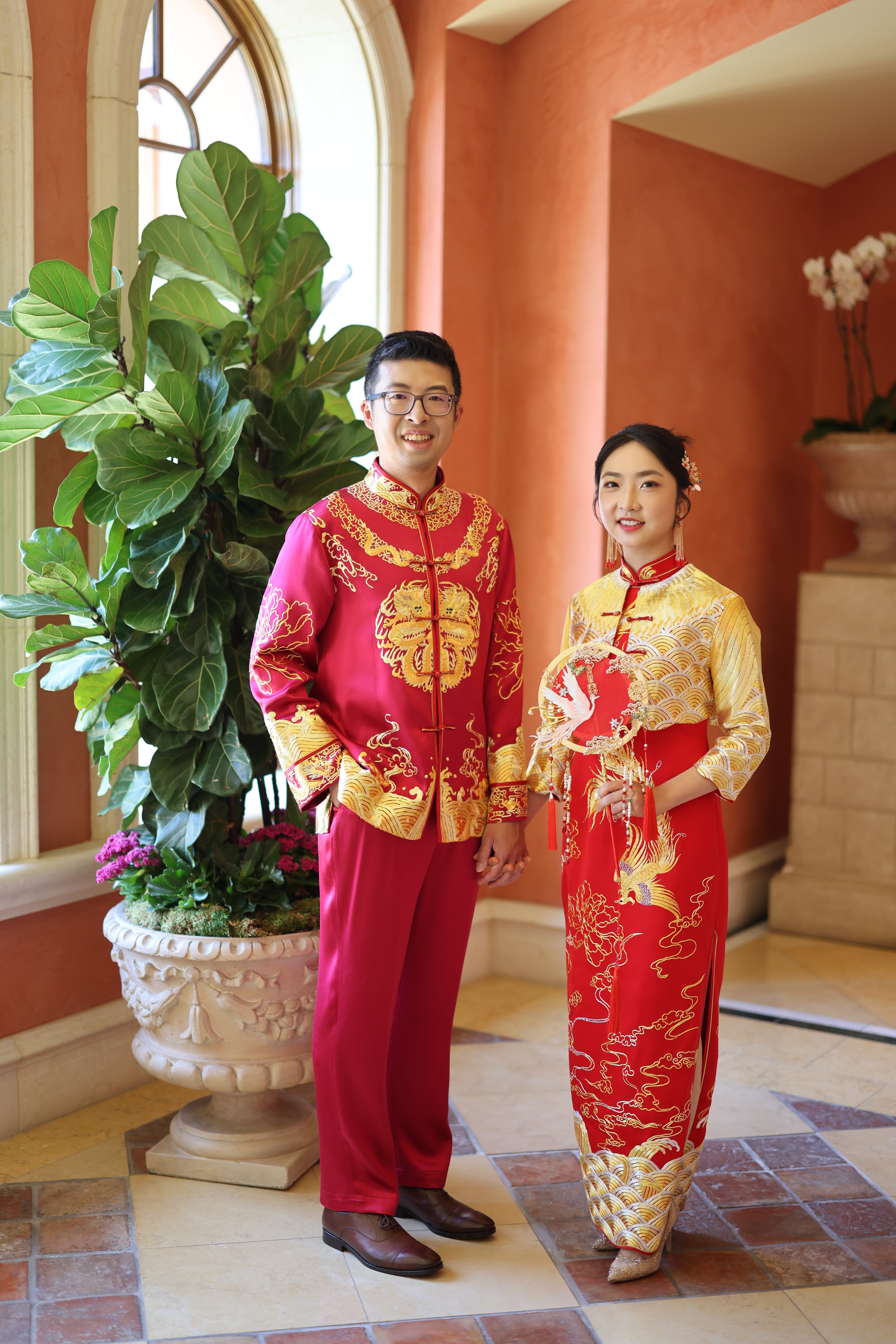 Front view of a groom wearing a luxurious red silk tang suit with 9 dragons embroidery, lucky cloud and sea wave, along with matching silk pants at his tea ceremony 