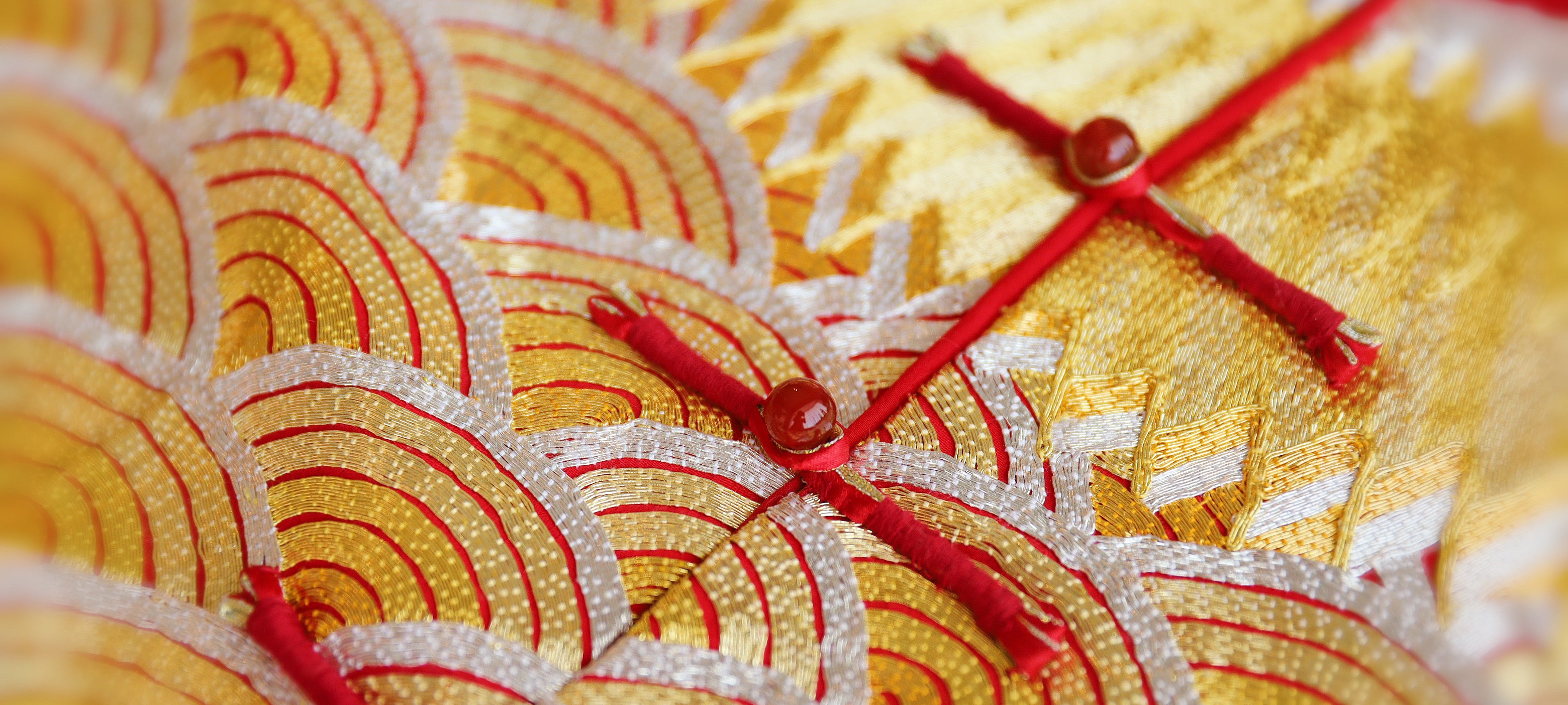 Close up of a 3-D hand-embroidered gold and silver lucky cloud and frog knot buttons on a Qun Kwa jacket. 