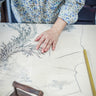 An embroiderer is drawing a phoenix pattern on the Qipao