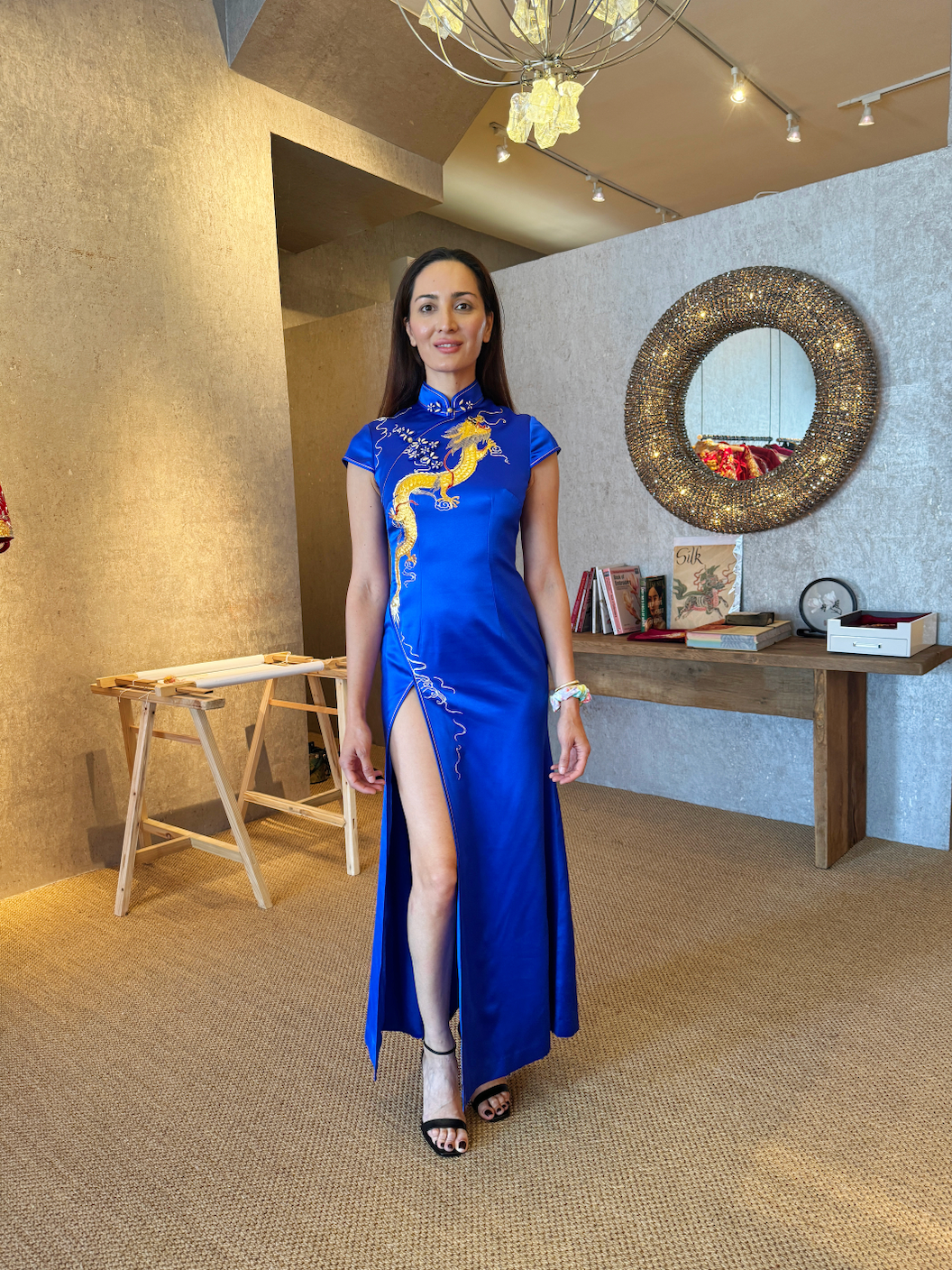 A woman wearing royal blue mermaid qipao with gold dragon hand embroidery with a front slit