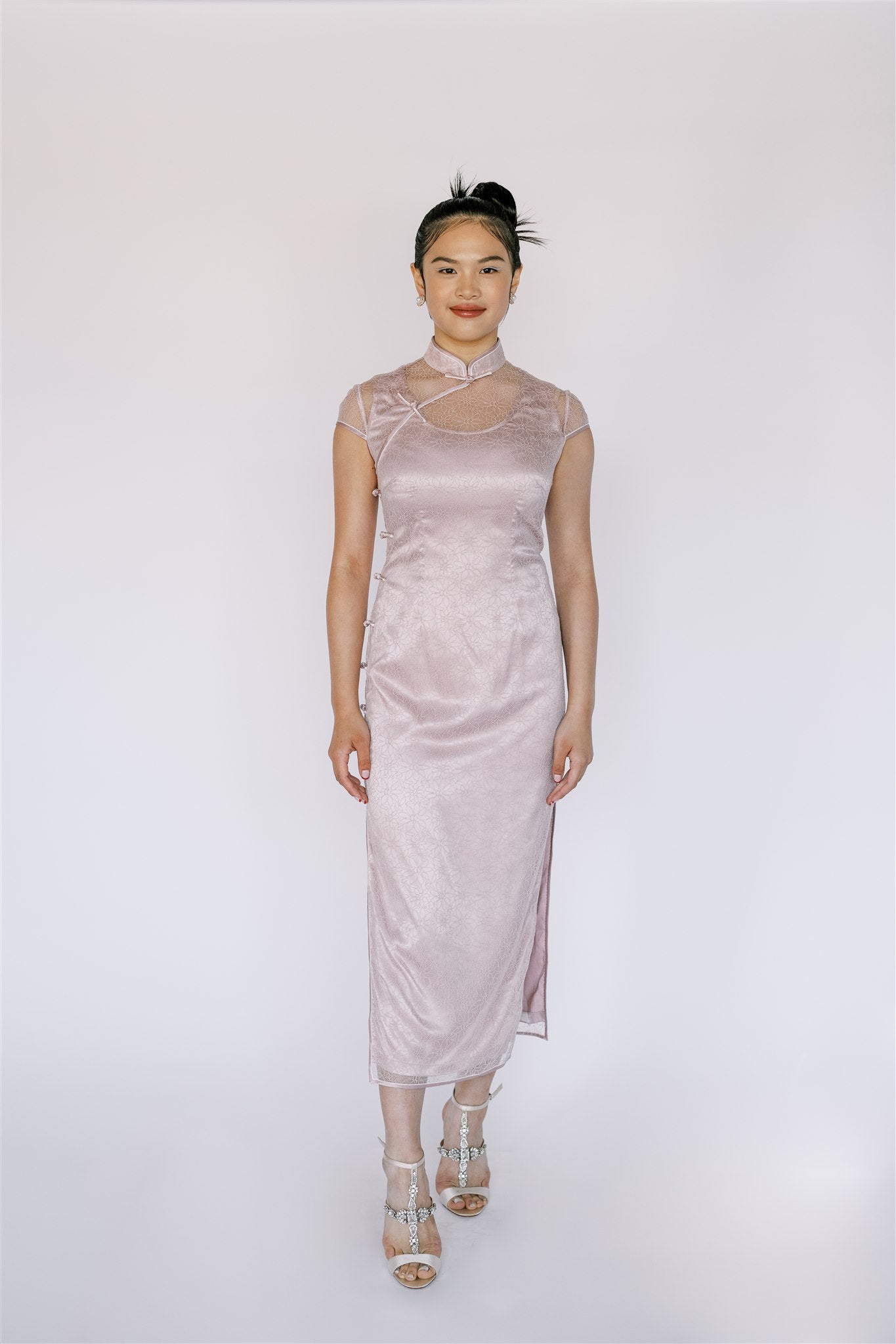 Front view of a Chantilly lace Cheongsam in blush pink. It is a delicate, sophisticated look, and ideal for formal occasions like graduation or weddings. 