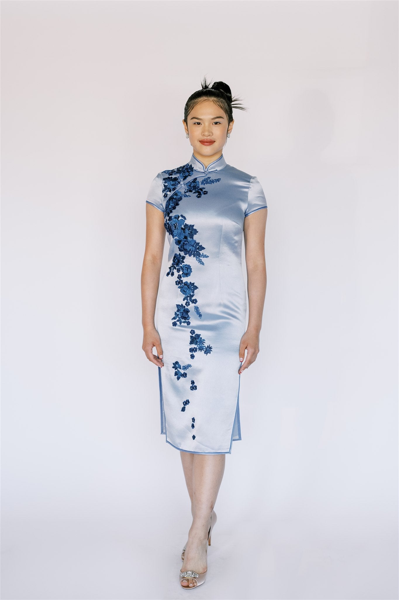 A front view of an elegant blue silk Cheongsam, it is a contemporary Qipao with delicate floral embellishments.