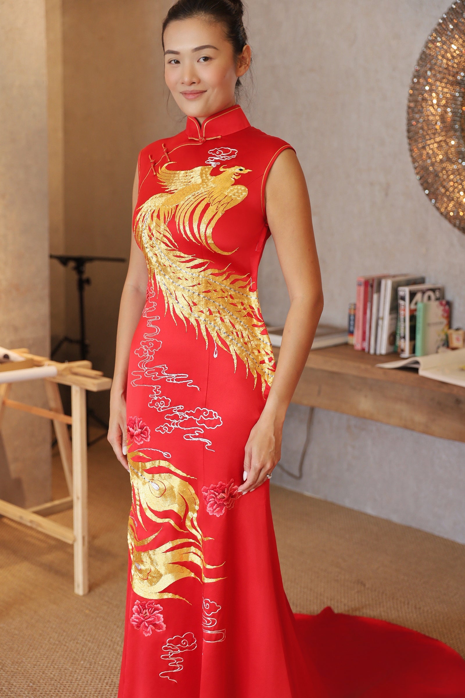 Side view of a modern red mermaid Cheongsam wedding dress with a train, gold phoenix embroidery wrapping around the body, and sleeveless style.