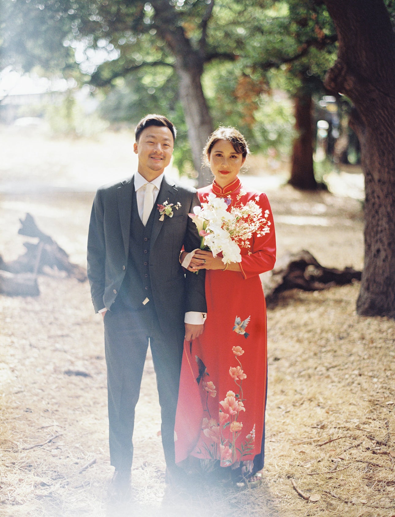 Front view of a bride wearing red Ao Dai, 3/4 sleeves, blue pants with floral embroidery at her wedding. 