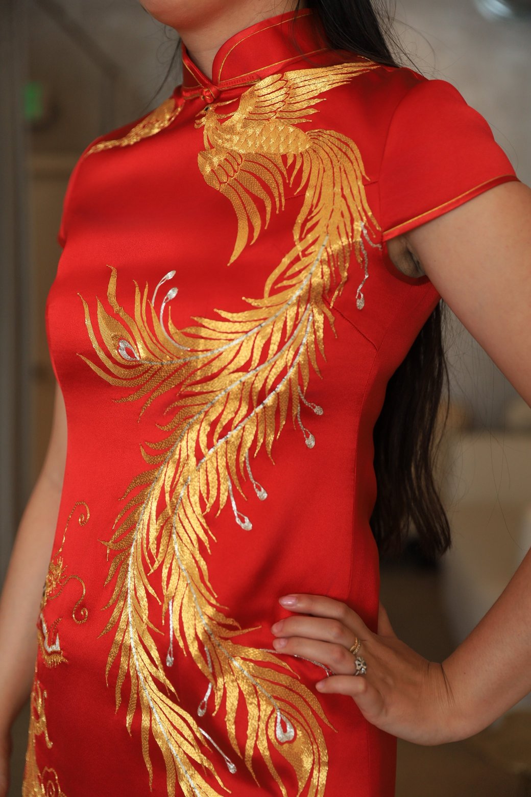 Close-up view of gold phoenix hand embroidery details on a red wedding Qipao