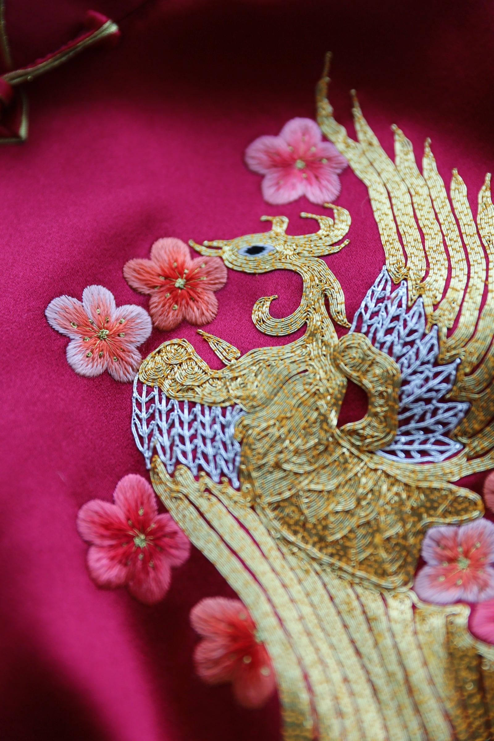Phoenix embroidery detail on wine red silk Qipao symbolizing grace and renewal.