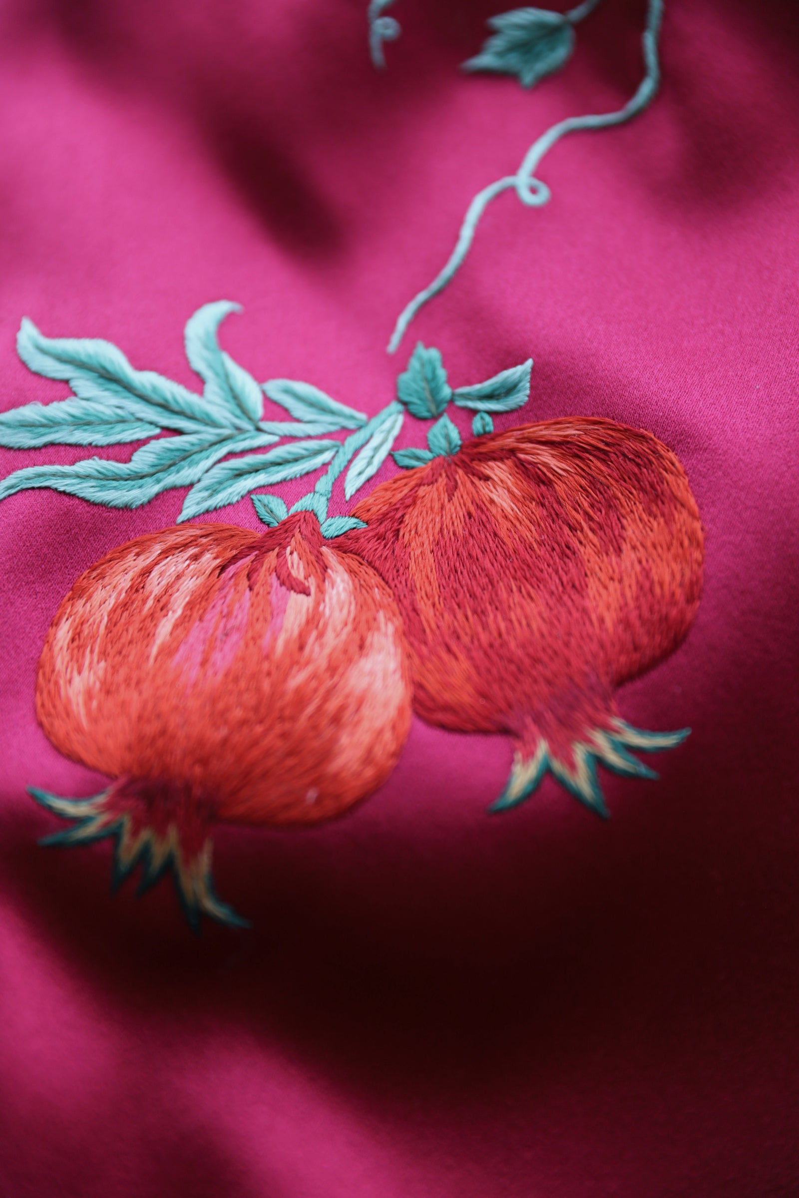 Pomegranate embroidery detail symbolizing prosperity on wine red silk Qipao.