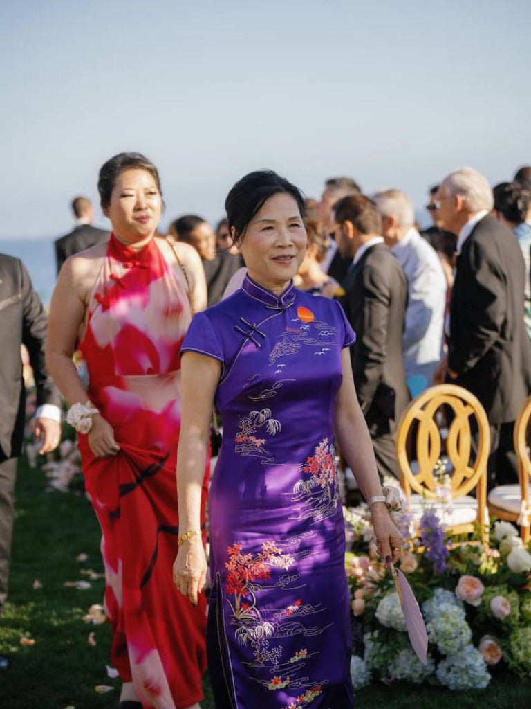 Front view of a mother is wearing a bespoke purple Qipao with trees and sun embroidery to her son's wedding. 